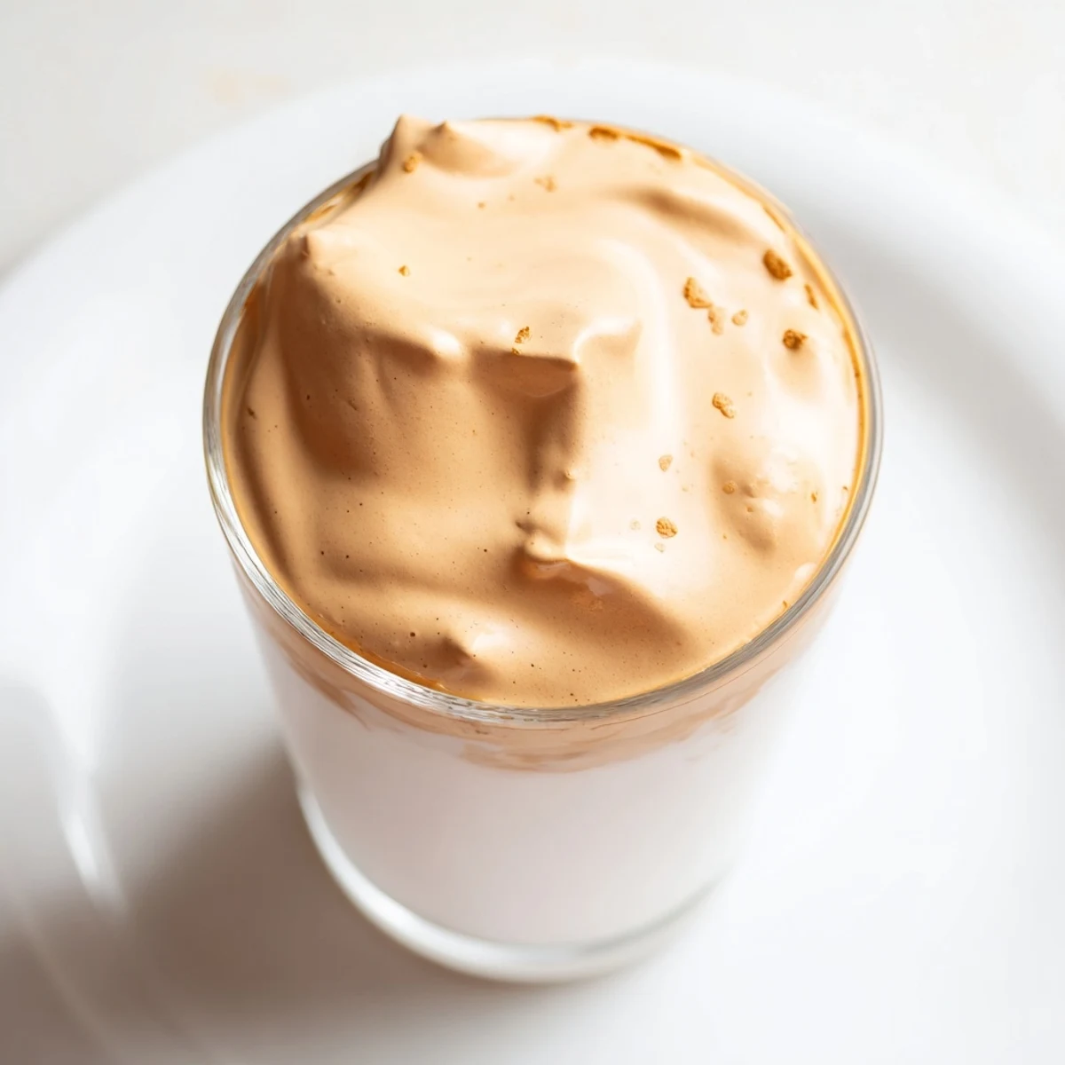 Fluffy whipped Dalgona coffee swirling atop cold milk, a rich and creamy café treat at home.