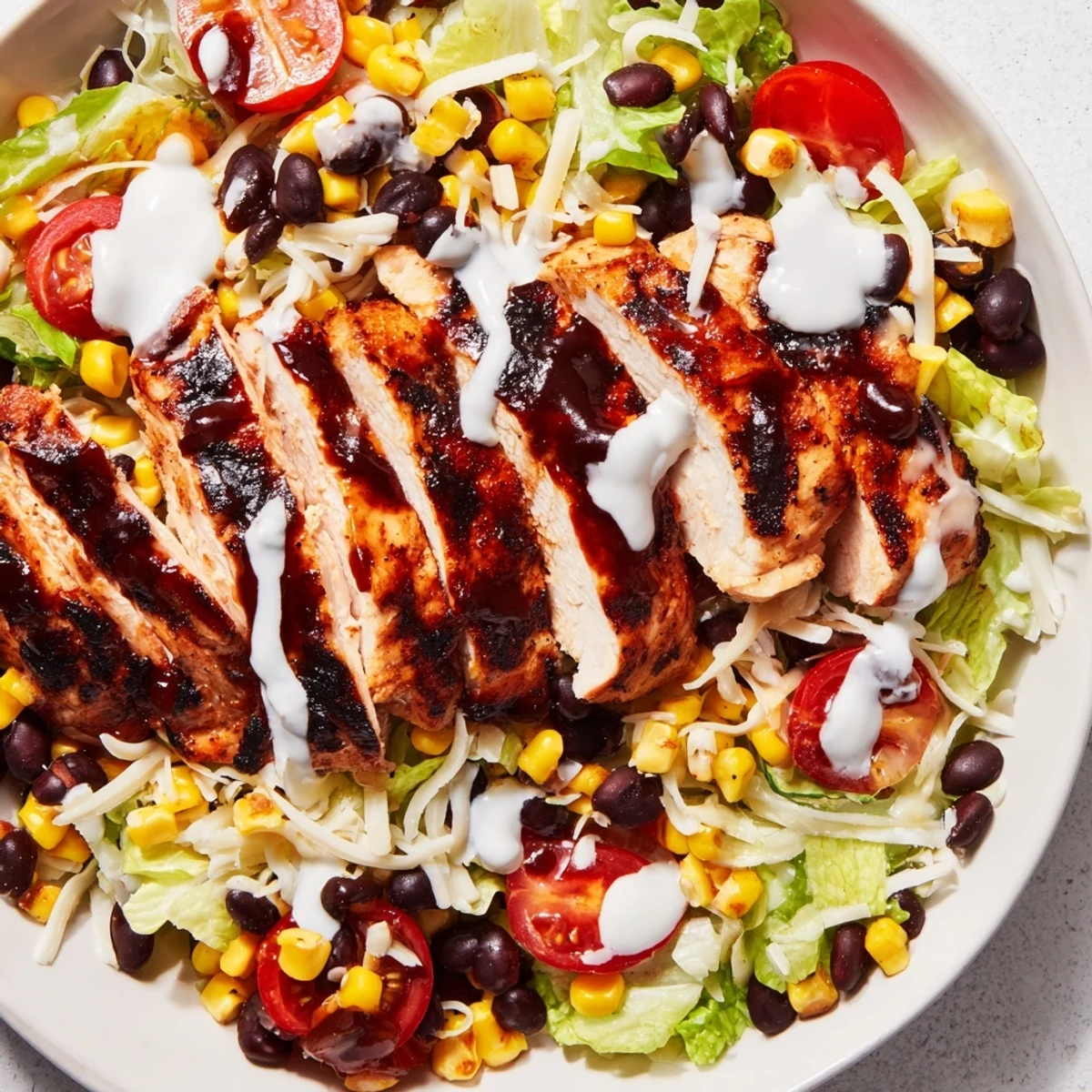 Top-down view of a hearty BBQ Chicken Salad with grilled corn, black beans, avocado, and cherry tomatoes, served in a white bowl.