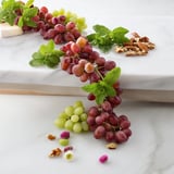Juicy red and green grapes cascade over a wooden board, ready to be enjoyed as a refreshing snack.