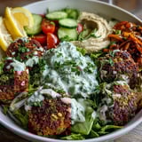 Golden falafel balls sit atop a bed of mixed greens, cherry tomatoes, and cucumber in this colorful Mediterranean-inspired bowl.