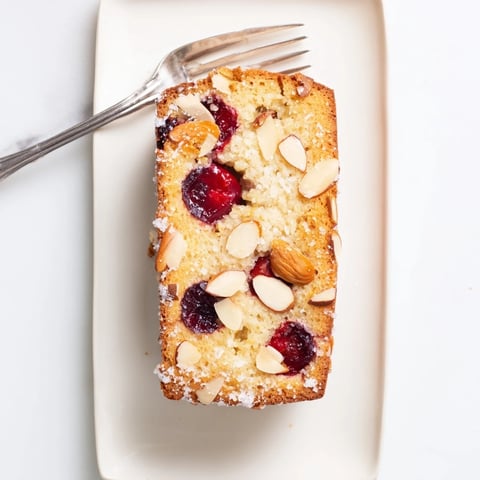 A freshly baked Cherry Almond Loaf Cake, boasting a golden crust and glistening, sweet cherries.
