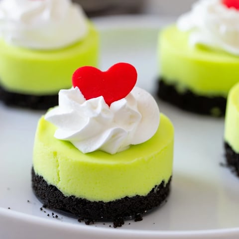 Bright green Grinch Mini Cheesecakes topped with fluffy whipped cream and festive heart sprinkles.