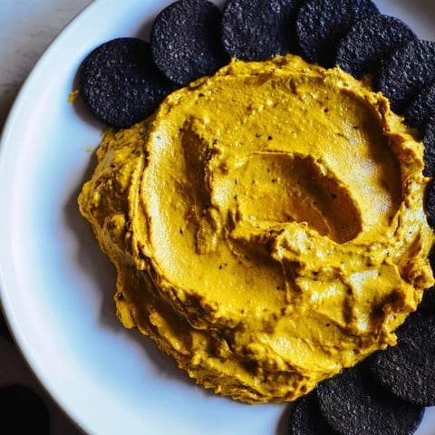 Picture of The Midnight Sun appetizer: creamy carrot dip encircled by dark charcoal crackers.