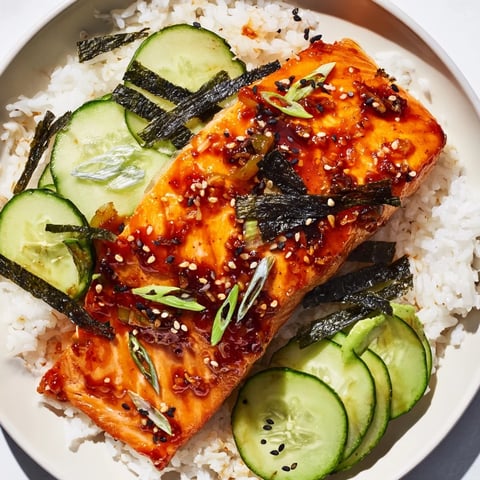 Tender Emily Mariko-Inspired Sticky Orange Gochujang Salmon Bowl, glistening with a vibrant glaze, sits atop fluffy rice.
