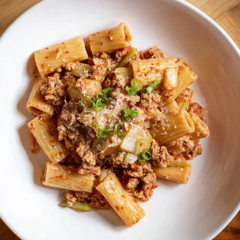 Steaming bowl of Chaos Cooking Kimchi Ragu Pasta, ready to serve with fresh green scallion garnish.