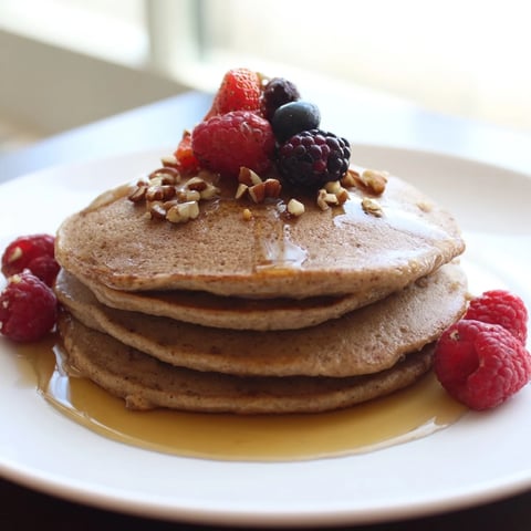 Fluffy brown banana pancakes, golden and ready, topped with fresh berries and maple syrup.