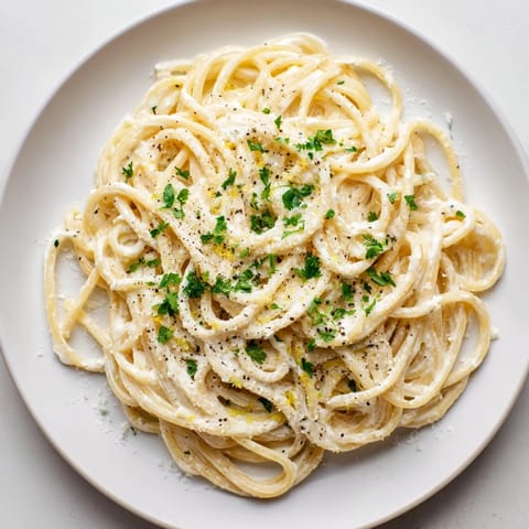 A close-up of Lemon Ricotta Pasta on a rustic board, showing creamy ricotta sauce clinging to al dente spaghetti and a wedge of lemon.  