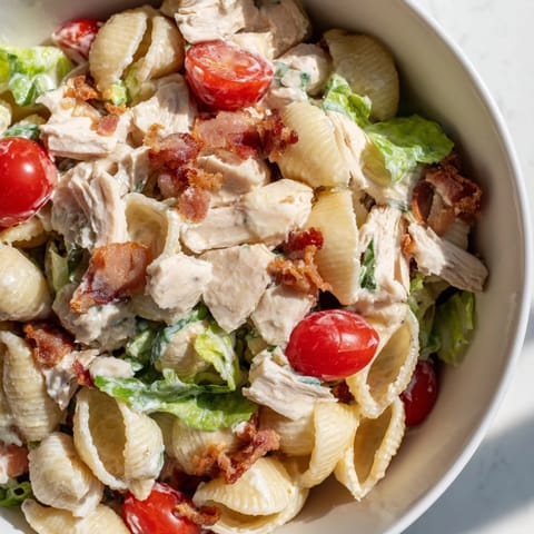 Chilled BLT Chicken Pasta Salad on a picnic table features tender pasta shells, smoky bacon crumbles, and halved cherry tomatoes for a summer lunch.