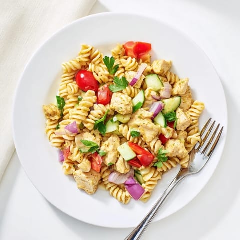 Colorful honey mustard chicken pasta salad with cherry tomatoes, cucumbers, and red bell pepper on a plate. 