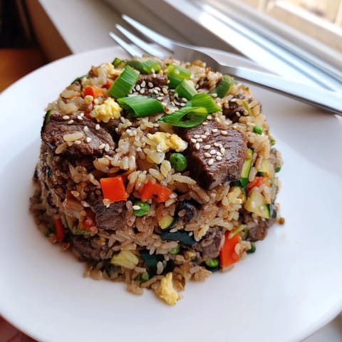 A sizzling skillet of Easy Hibachi Steak With Fried Rice, garnished with fresh green onions and sesame seeds.  