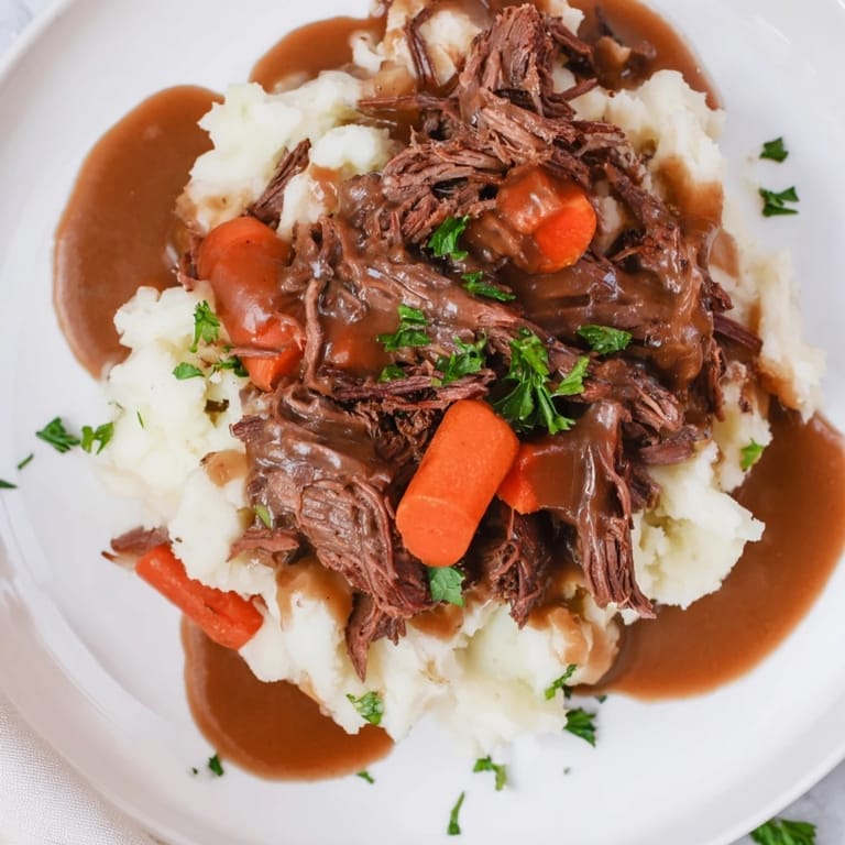 A close-up of a richly flavored, fall-apart pot roast resting atop fluffy mashed potatoes.