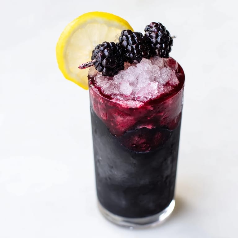 A visually stunning Dark Matter Mocktail, a vegan, gluten-free beverage, features black layers with berry and citrus garnishes.