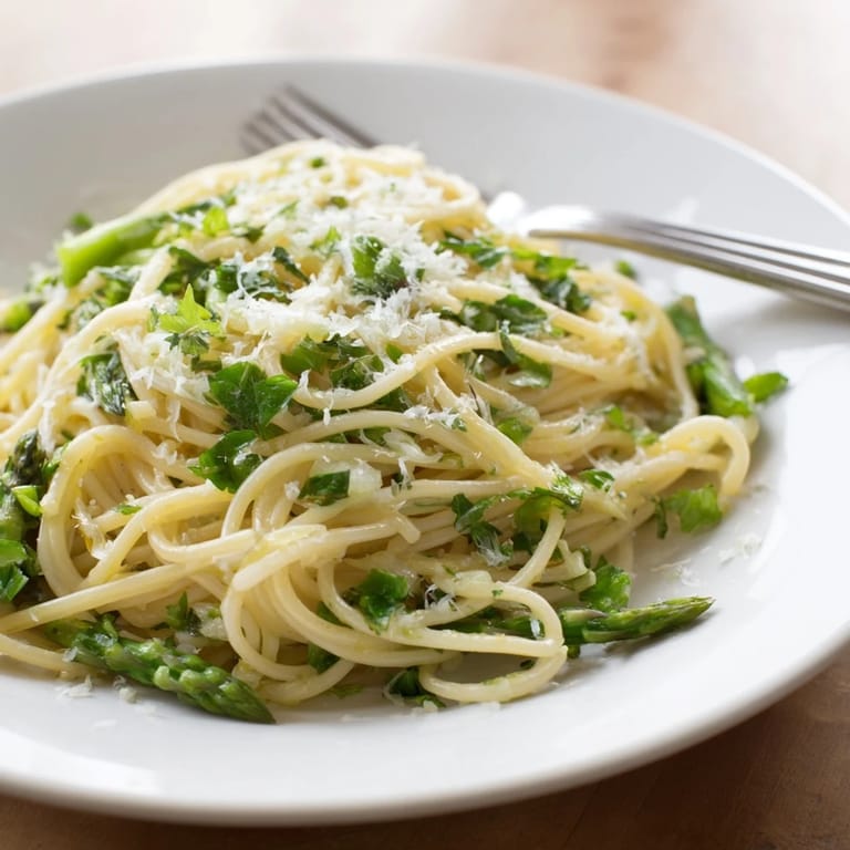 Overhead view of Roasted Garlic & Asparagus Pasta in a white bowl, garnished with Parmesan and parsley, ready for a vegetarian spring dinner.