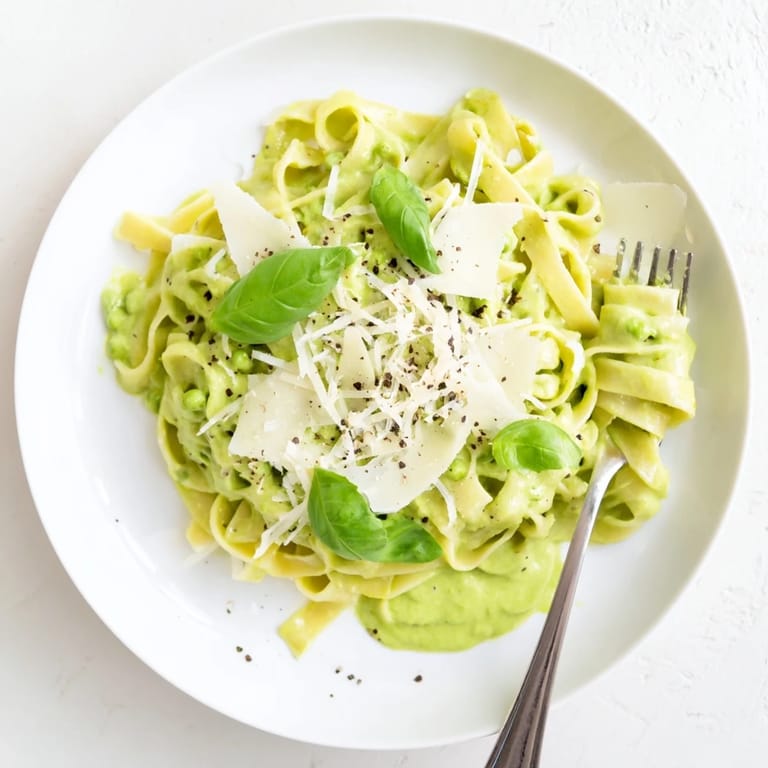 Overhead view of a serving of Creamy Green Pea Alfredo, garnished with fresh basil and grated Parmesan cheese.