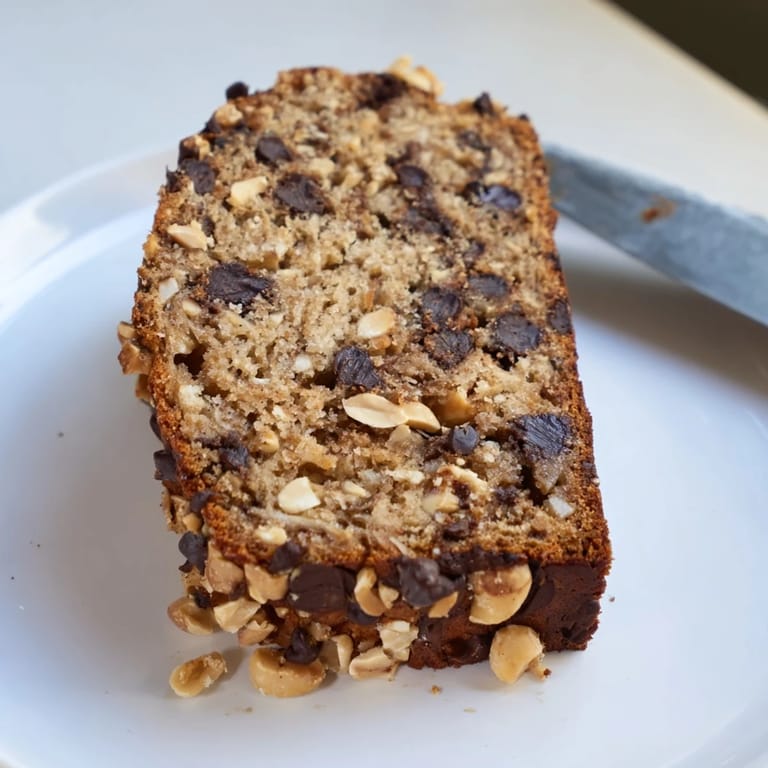Warm slice of Chocolate Chip Peanut Butter Oatmeal Banana Bread on a plate with a dollop of creamy peanut butter and a glass of milk for breakfast.